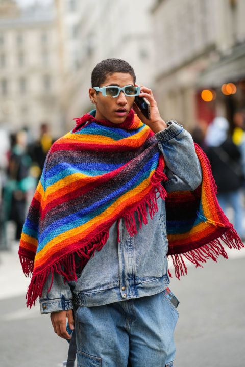 man with blue sunglasses holding phone and rainbow scarf inspo for what to wear to pride 2022