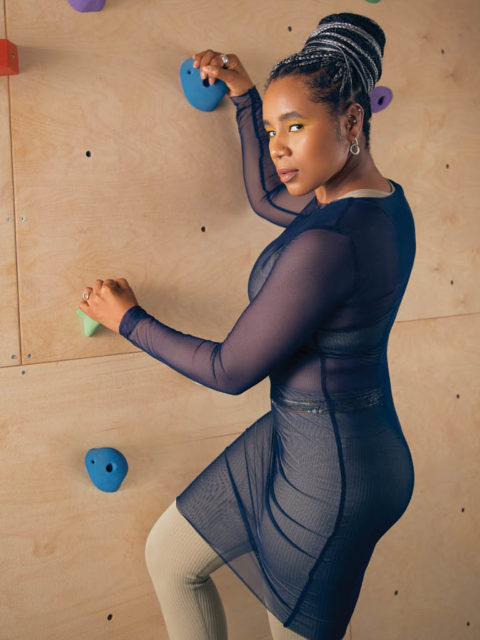 woman poses in sheer bodysuit by a rock climbing wall