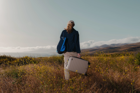 woman in a field holding a carry-on suitcase filled with travel essentials